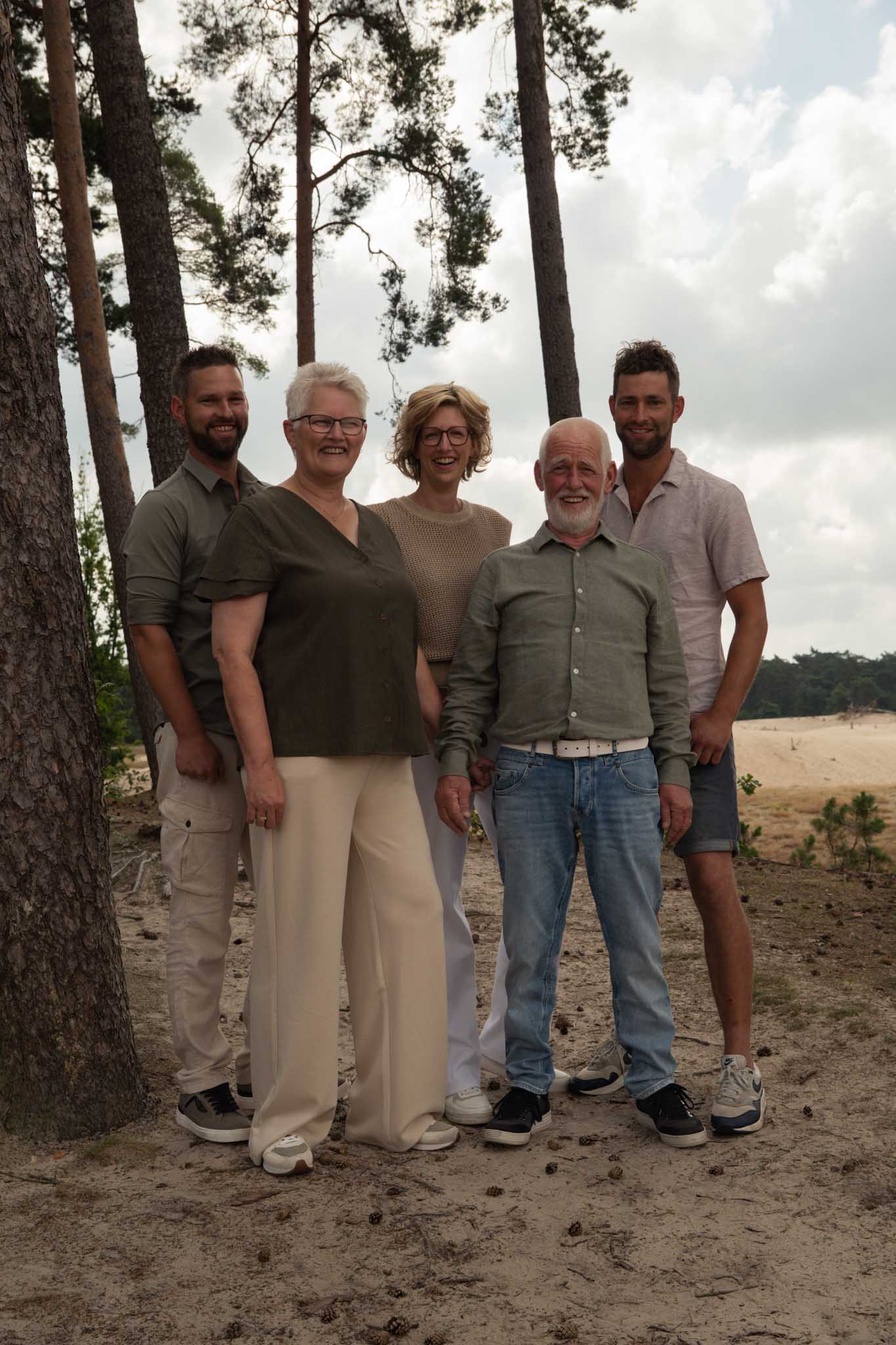 Een familie kijkt lachend naar de camera staand naast een boom op een zandvlakte