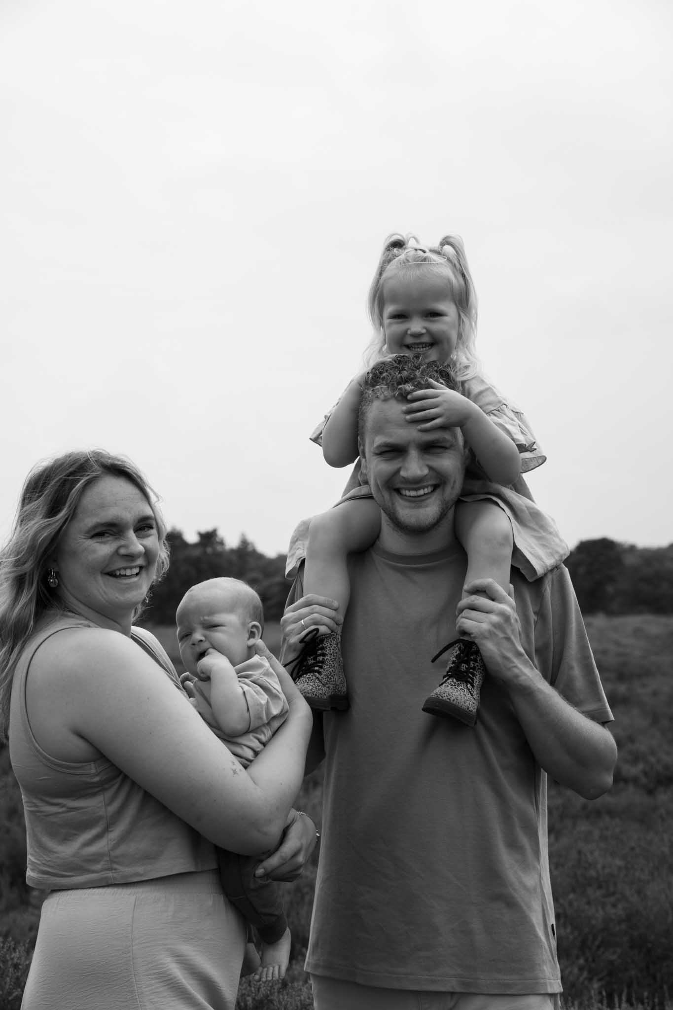 Een zwart-wit afbeelding van een vader, moeder, kind en baby in de weide