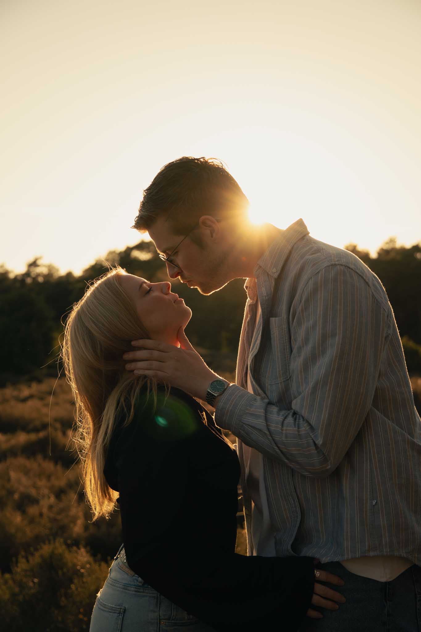 Een koppel rijkt elkaar de mond met een ondergaande zon op de achtergrond