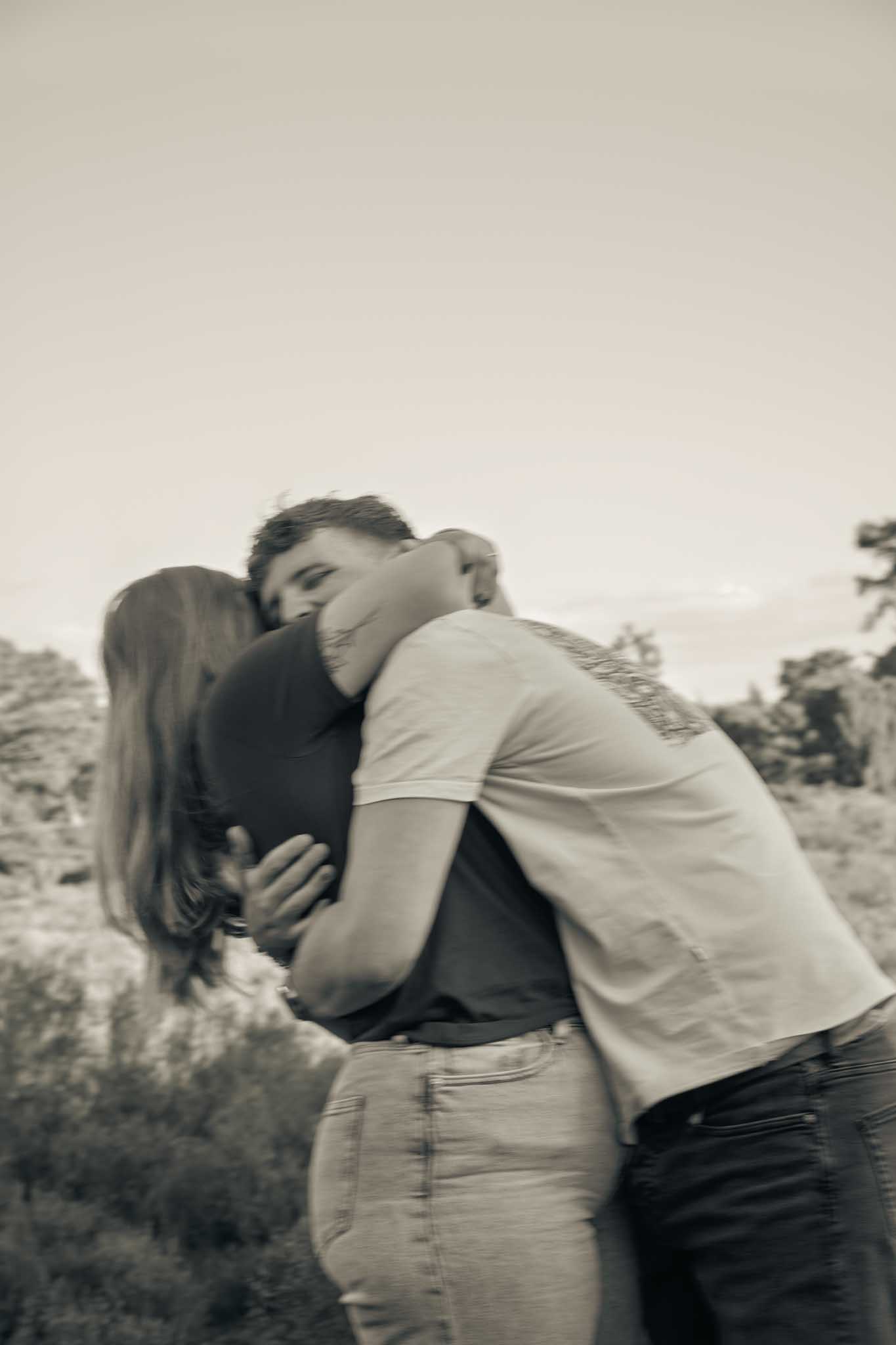 Een koppel zit in het zand waarbij de man lachend naar de camera kijkt en de vrouw lachend tegen de man aan leunt