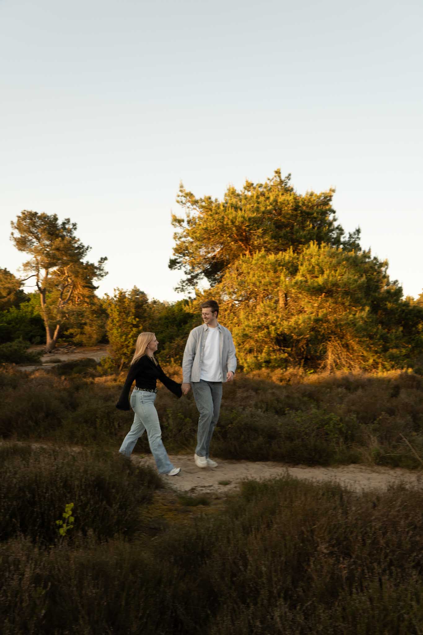 Een stel loopt hand in hand, kijkend naar elkaar, over een zandpad in de heide