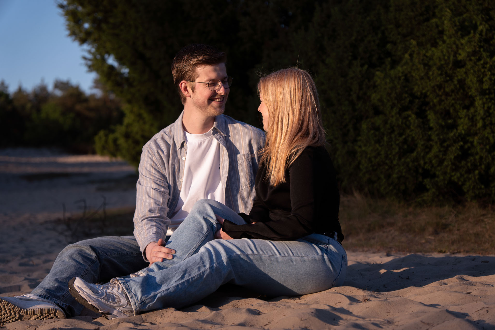Een koppel kijkt elkaar lachend aan zittend in het zand