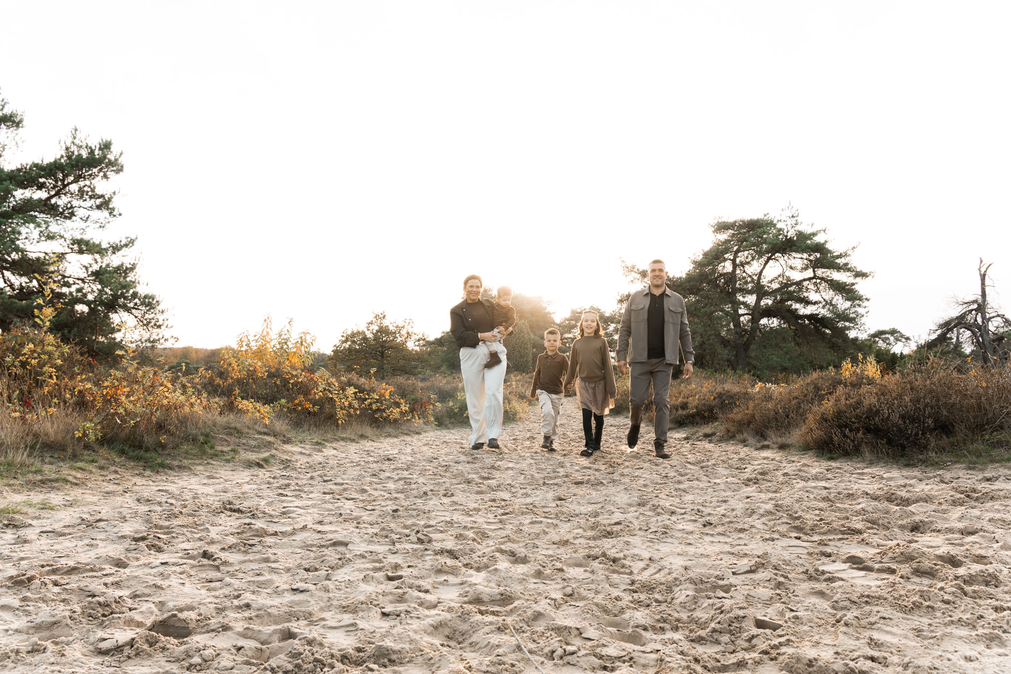 liggende foto van een jong gezin met pas geboren baby. ouders kijken lachend naar de baby die bij moeder in de armen ligt. ze staan buiten met de mooie heide als achtergrond